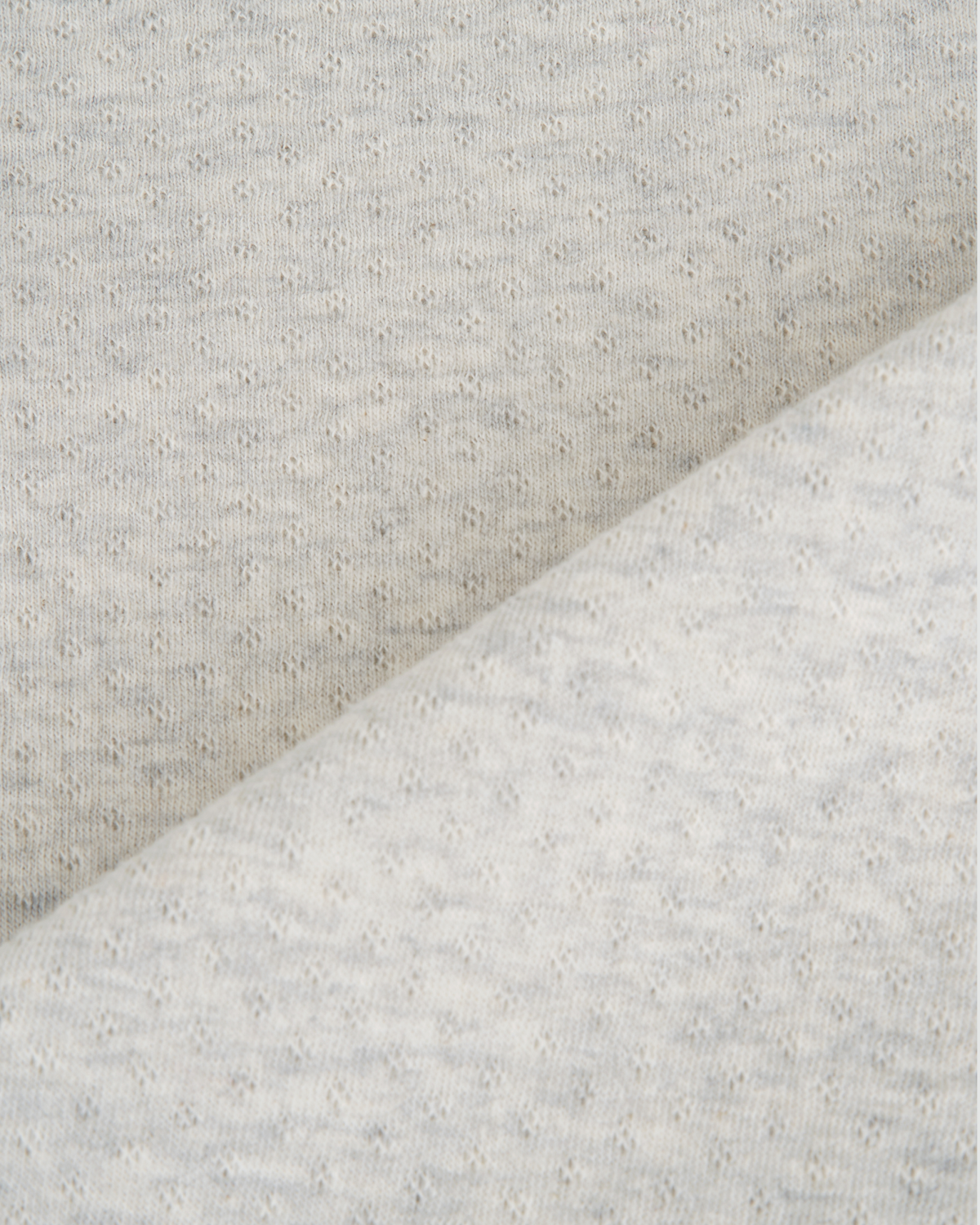 Close-up of a light gray heathered fabric with a eyelet dotted texture, folded diagonally to show the material's softness and color.