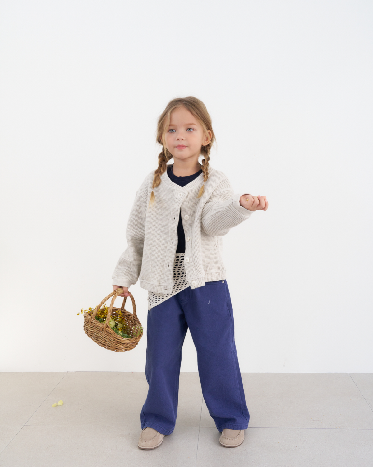 Girl wearing The Fruto Natural Button Cardigan in Oat, a textured waffle-knit cardigan styled with a dark top and wide-leg navy pants.