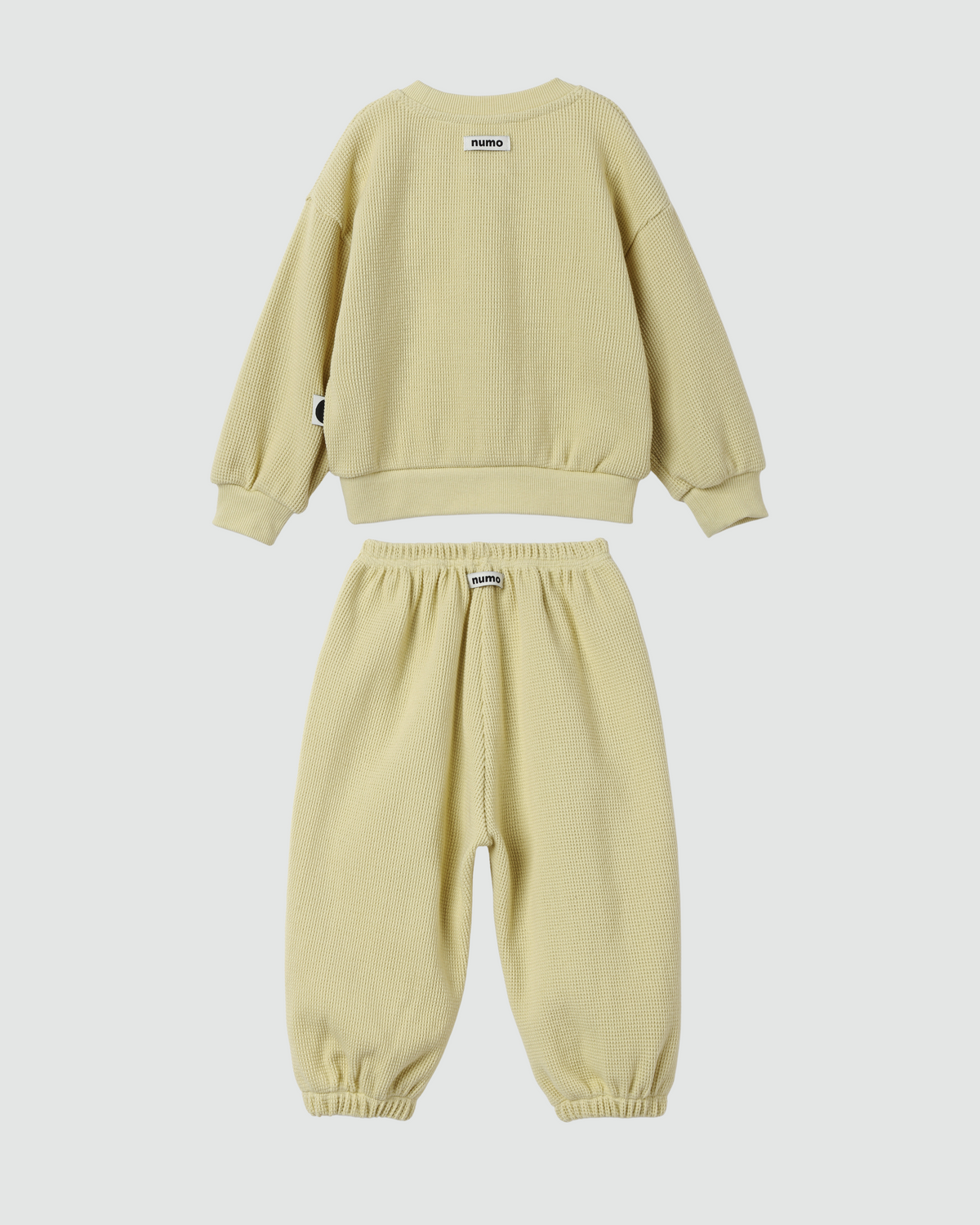 A two-piece children's sweatpants set in pale yellow, featuring a long-sleeve sweatshirt and matching jogger pants with elastic cuffs, shown against a light gray background.